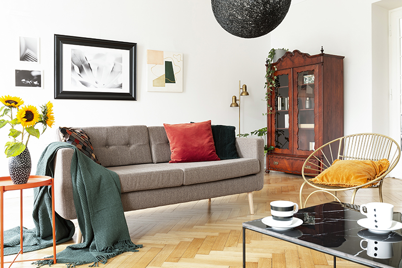 Armchair next to couch with blanket in white apartment interior with sunflowers and posters.